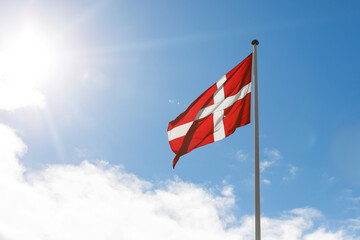 Danish flag waving on the blue sky sun glare background.