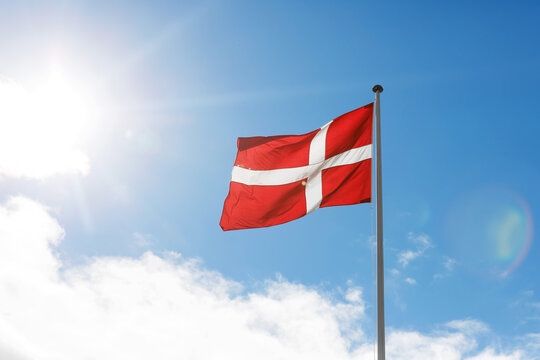 Danish flag waving on the blue sky sun glare background.