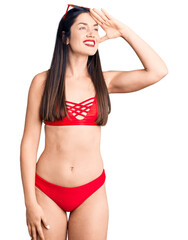 Fototapeta premium Young beautiful caucasian woman wearing bikini very happy and smiling looking far away with hand over head. searching concept.