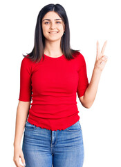 Young beautiful girl wearing casual t shirt smiling with happy face winking at the camera doing victory sign. number two.