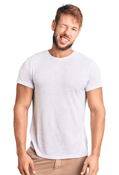 Young caucasian man wearing casual white tshirt winking looking at the camera with sexy expression, cheerful and happy face.
