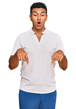 Young arab man wearing casual clothes pointing down with fingers showing advertisement, surprised face and open mouth