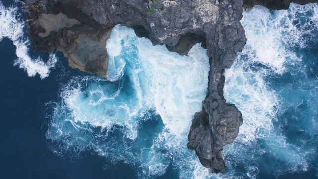 Top shot of beautiful swirling tidal waves in a small bay with caves of rock in tropical water. Ocean power rotating maelstrom. Wild sea washing cliff with arch. Beautiful aerial background of nature.
