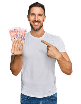 Handsome man with beard holding south african 50 rand banknotes smiling happy pointing with hand and finger