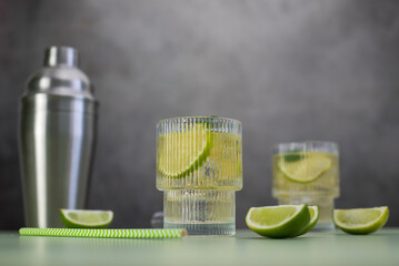 two fresh cold glasses of mahito with lime and ice and shaker on a gray-green background.