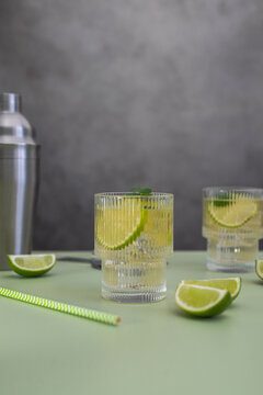 two fresh cold glasses of mahito with lime and ice and shaker on a gray-green background.