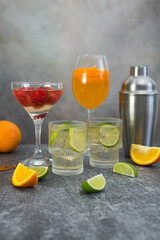 assorted cocktails: two glasses of mojito, orange cocktail, cocktail with strawberries, fruits and shaker on a gray background.