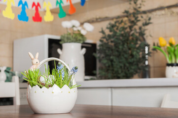 Basket with spring grass and Easter eggs on table on background of decorated kitchen. Spring kitchen decor for Easter