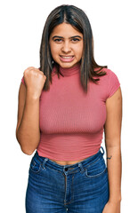 Young hispanic girl wearing casual t shirt angry and mad raising fist frustrated and furious while shouting with anger. rage and aggressive concept.