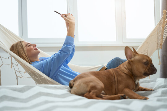 Joyous woman photographing herself with smartphone while her pet resting