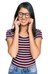 Beautiful asian young woman wearing casual clothes and glasses covering ears with fingers with annoyed expression for the noise of loud music. deaf concept.