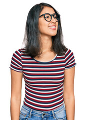 Beautiful asian young woman wearing casual clothes and glasses looking away to side with smile on face, natural expression. laughing confident.