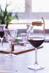 A wine thermometer on a glass of red wine, with elegant glasses of wine in the background