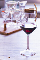 A wine thermometer on a glass of red wine, with elegant glasses of wine in the background