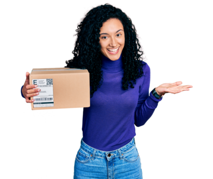 Young hispanic woman with curly hair holding delivery package celebrating achievement with happy smile and winner expression with raised hand