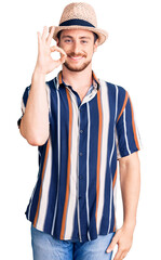 Young handsome caucasian man wearing summer hat smiling positive doing ok sign with hand and fingers. successful expression.