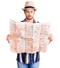 Young handsome caucasian man wearing summer hat holding city map thinking attitude and sober...