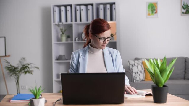 charming woman checks work done by students or interns sitting at computer in home office, remote work