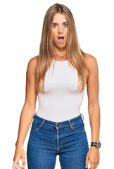 Young blonde woman wearing casual style with sleeveless shirt in shock face, looking skeptical and sarcastic, surprised with open mouth