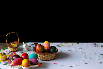 Colored easter eggs in a wooden basket at a white tablecloth on a black background