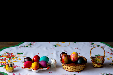 Colored easter eggs in a wooden basket at a white tablecloth on a black background