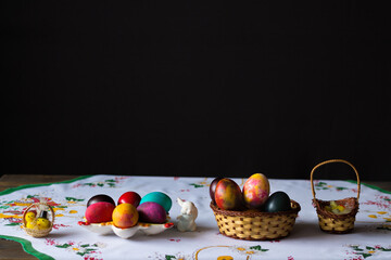 Colored easter eggs in a wooden basket at a white tablecloth on a black background