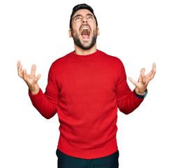 Naklejka premium Young hispanic man wearing casual clothes crazy and mad shouting and yelling with aggressive expression and arms raised. frustration concept.