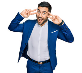 Young hispanic man wearing business jacket doing peace symbol with fingers over face, smiling cheerful showing victory