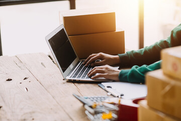 Startup SME small business entrepreneur of freelance Asian woman wearing apron using laptop and box to receive and review orders online to prepare to pack sell to customers, online sme business ideas.