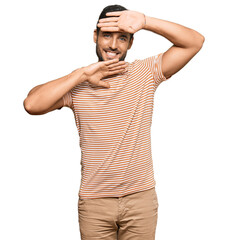 Handsome hispanic man wearing casual clothes smiling cheerful playing peek a boo with hands showing face. surprised and exited