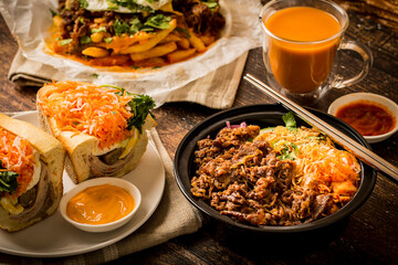 Vietnamese food - Korean style beef bulgogi bowl with ham headcheese BBQ pork sandwich, Kimchi fries, and thai iced tea on the wooden table