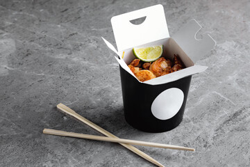 Chinese food in a black takeout box on a gray background. Sushi chopsticks and a black box.