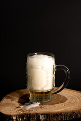 Cerveza fría y espumosa en vaso cervecero sobre tronco de madera en fondo negro - Cold foamy beer in pint glass on wooden log on black background
