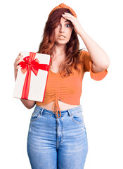 Young beautiful woman holding gift stressed and frustrated with hand on head, surprised and angry face