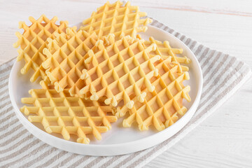 Ferratelle or pizzelle a traditional dessert or cookies on a plate on a white wooden background, close up. Regional cuisine of Abruzzo, Italy. Like the well-known waffle