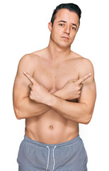 Fototapeta premium Handsome young man wearing swimwear shirtless pointing to both sides with fingers, different direction disagree