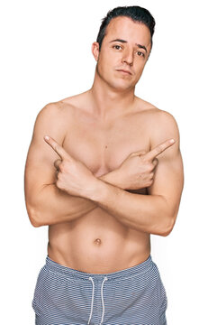 Handsome young man wearing swimwear shirtless pointing to both sides with fingers, different direction disagree