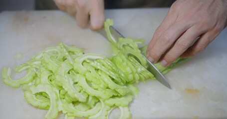 close up man hands cutting slices fresh organic green bitter melon into smaller pieces with kitchen knife on cutting board at the kitchen, preparing cooking food