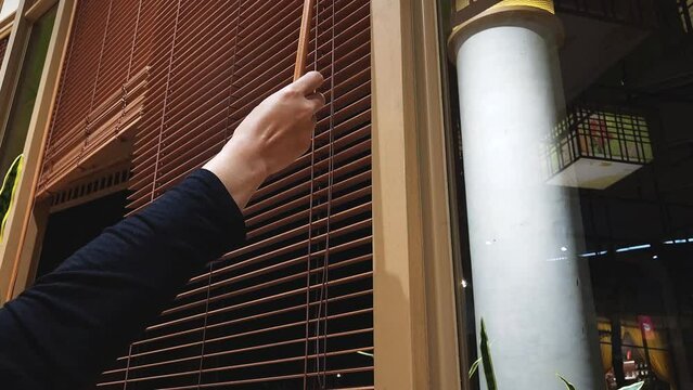 someone closes the wooden blinds by turning