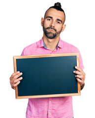 Hispanic man with ponytail holding blackboard relaxed with serious expression on face. simple and natural looking at the camera.