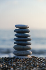 Vertical İmage of balanced pebble pyramid at the beach. Selective focus Abstract bokeh with Sea on the background. Zen stones on the beach, meditation, spa, harmony, calmness, balance concept.