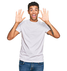 Naklejka premium Young handsome african american man wearing casual white tshirt showing and pointing up with fingers number ten while smiling confident and happy.