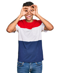 Young handsome african american man wearing casual clothes doing ok gesture like binoculars sticking tongue out, eyes looking through fingers. crazy expression.