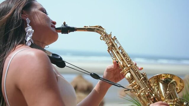 A beautiful woman stands in a white dress and plays a golden saxophone