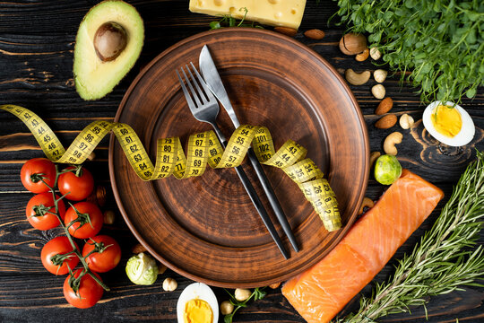 The concept of healthy eating and diet. A set of products of the low-carb keto diet. Plate with knife and fork with measuring tape. Top view