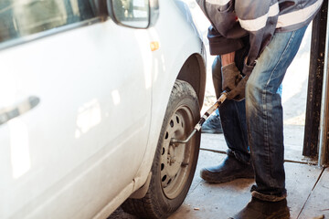 Mechanic changing a car tire in a workshop on a car using an electric drill to loosen the bolts