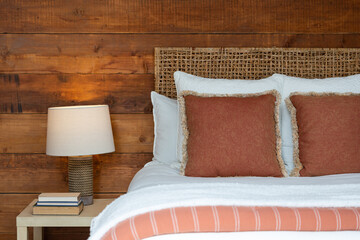 Country bedroom details of bed with white and orange linens, side table with lamp and wood slat wall covering.