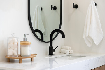 Modern bathroom details of sink with black faucet, black rim mirror, white towel hanging on black...