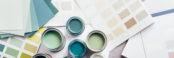 Tiny sample paint cans during house renovation, process of choosing paint for the walls, different green and beige colors, color charts on background, banner size