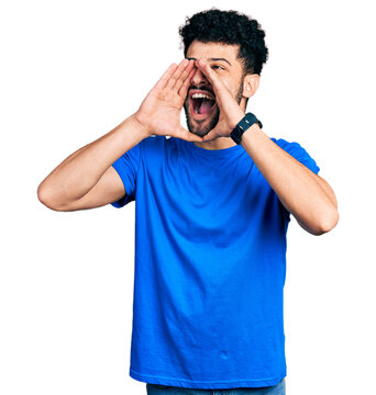 Young arab man with beard wearing casual blue t shirt shouting angry out loud with hands over mouth